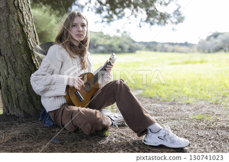 Young musician playing ukulele under a tree in nature 130741023