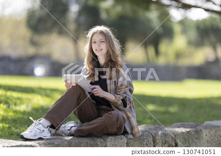 Teenage student girl taking notes while studying outdoors in park 130741051