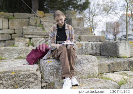 Student writing notes outdoors on stone steps 130741163