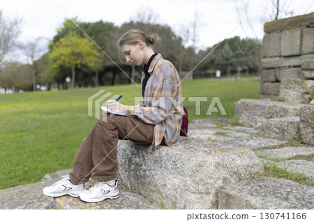 Young woman writing on notebook outdoors in archaeological site 130741166