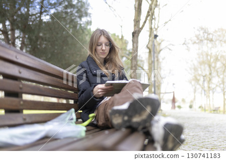 Young woman reading book on park bench after rain Young woman reading book on park bench after rain 130741183