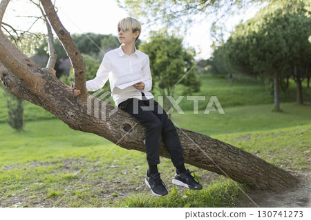Young student studying outdoors sitting on a tree branch in a park Young student studying outdoors sitting on a tree branch in a park 130741273