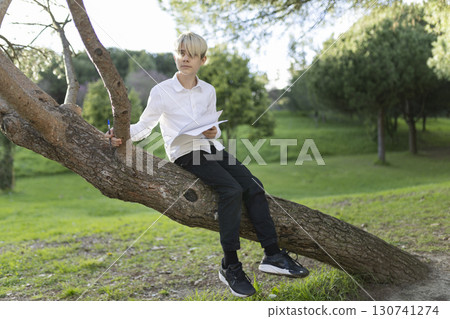 Young student studying outdoors sitting on a tree branch in a park 130741274