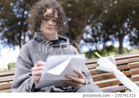 Young man writing on a bench in a park 130741313