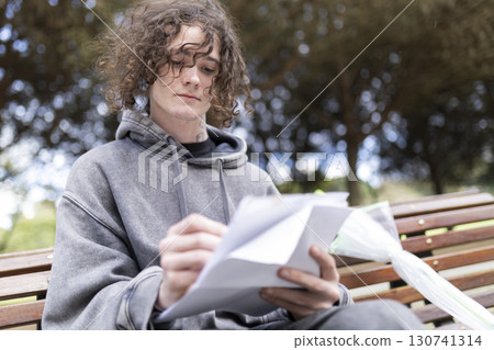 Young man reading documents on park bench Young man reading documents on park bench 130741314