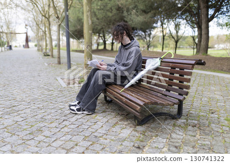 Young man writing on a bench in a park with umbrella 130741322
