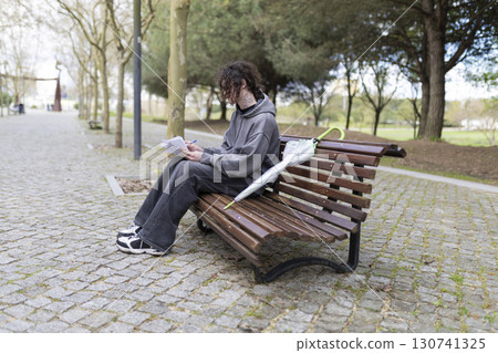 Young man writing on a bench in the park with umbrella 130741325
