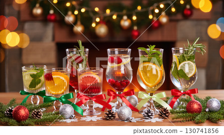 Christmas festive drinks in elegant glasses with citrus, cranberries, mint, and rosemary decorated with ribbons, ornaments, and glowing holiday lights 130741856