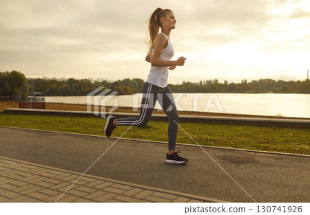 Cheerful slim girl athlete is exercising during morning run in fitness outfit. 130741926