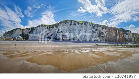 Panoramic view of Dieppe beach in Normandy, France. Majestic white chalk cliffs rise above a pebble shore, with the low tide revealing a vast expanse of wet sand reflecting the blue sky Panoramic view of Dieppe beach in Normandy, France. Majestic white chalk cliffs rise above a pebble shore, with the low tide revealing a vast expanse of wet sand reflecting the blue sky 130741957