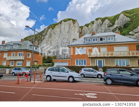 Row of houses with distinctive orange brickwork sits at the base of dramatic white chalk cliffs in Dieppe, France. Parked cars along the street with a red-toned bike lane in the foreground Row of houses with distinctive orange brickwork sits at the base of dramatic white chalk cliffs in Dieppe, France. Parked cars along the street with a red-toned bike lane in the foreground 130741958