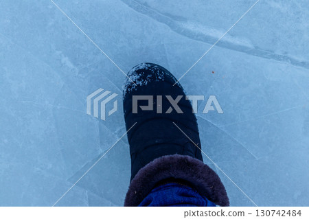 Foot standing on cracked natural lake ice texture. Concept of danger exit to badly frozen water 130742484
