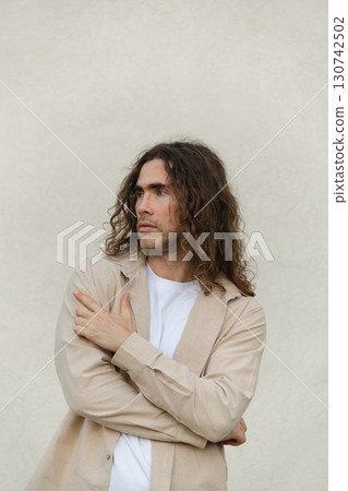 Handsome caucasian man with long hair wearing beige casual shirt stands against neutral background. Contemplation and introspection. Handsome caucasian man with long hair wearing beige casual shirt stands against neutral background. Contemplation and introspection. 130742502