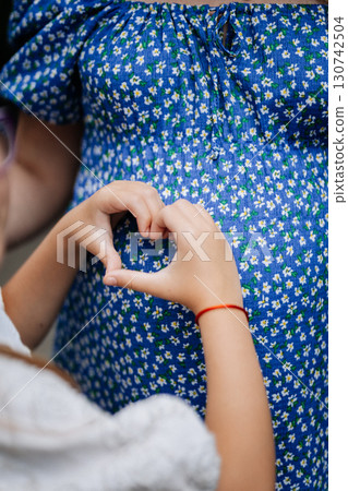 Child hands forming heart on pregnant belly, symbolizing love and family bond Child hands forming heart on pregnant belly, symbolizing love and family bond 130742504