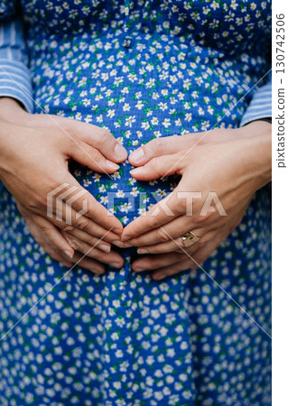 Pregnant couple holding hands on belly in heart shape, celebrating new life 130742506
