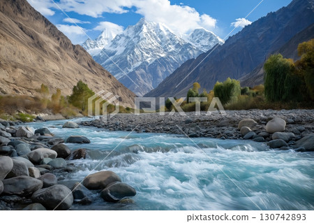 Turquoise mountain river flowing rapidly through a rocky gorge with a backdrop of snow capped mountains and autumnal trees Turquoise mountain river flowing rapidly through a rocky gorge with a backdrop of snow capped mountains and autumnal trees 130742893