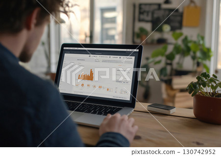 Businessman is analyzing financial data displayed on his laptop screen, deeply engrossed in his startup project within the comfortable setting of his office Businessman is analyzing financial data displayed on his laptop screen, deeply engrossed in his startup project within the comfortable setting of his office 130742952