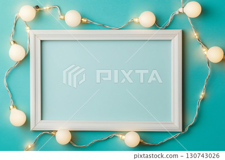 White empty photo frame surrounded by glowing garland on turquoise background creating festive atmosphere for Christmas and new year White empty photo frame surrounded by glowing garland on turquoise background creating festive atmosphere for Christmas and new year 130743026