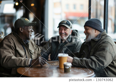 Three mature veterans share a joyful moment over coffee at a cozy cafe table, laughing, talking, and reminiscing about their experiences 130743062