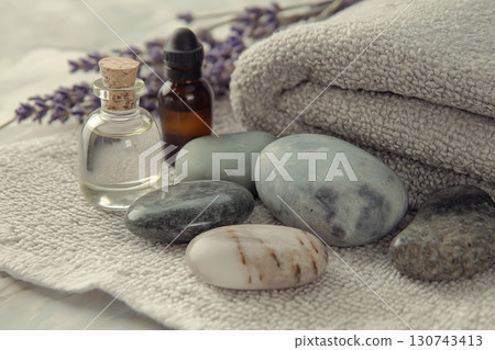 Massage stones and essential oils with lavender for spa treatment are lying on a towel, inviting to relaxation 130743413