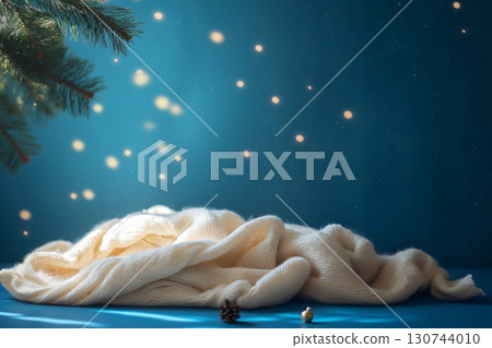 White knitted blanket illuminated softly on blue Christmas background with pine tree branch, perfect for product placement 130744010