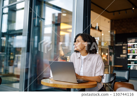 A Young Woman is Engaged in Working on Her Laptop in a Stylish Modern Coffee Shop 130744116