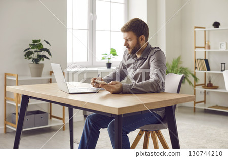 Focused businessman using smartphone and laptop computer at home office Focused businessman using smartphone and laptop computer at home office 130744210