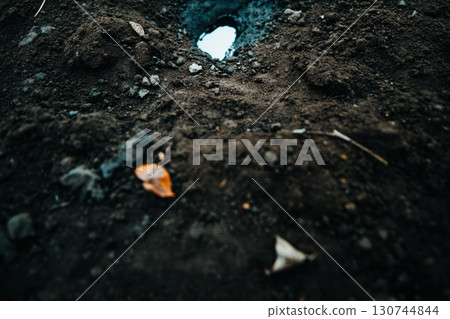 Dark soil with a striking blue hole revealing the sky above 130744844