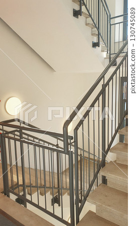 Internal staircase with marble stone beige stairs inside the building and metal railings. Internal staircase with marble stone beige stairs inside the building and metal railings. 130745089