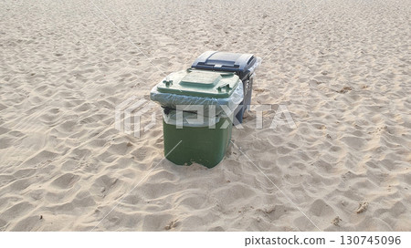 Green and black plastic waste containers buried in yellow sand on the beach. Ostend, Belgien. Green and black plastic waste containers buried in yellow sand on the beach. Ostend, Belgien. 130745096