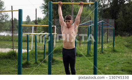 Muscular athlete doing pull ups on horizontal bar at sports ground. Young shirtless sportsman exercising at nature. Strong sporty man training outdoor. Concept of healthy and active lifestyle. Slow mo Muscular athlete doing pull ups on horizontal bar at sports ground. Young shirtless sportsman exercising at nature. Strong sporty man training outdoor. Concept of healthy and active lifestyle. Slow mo 130745330