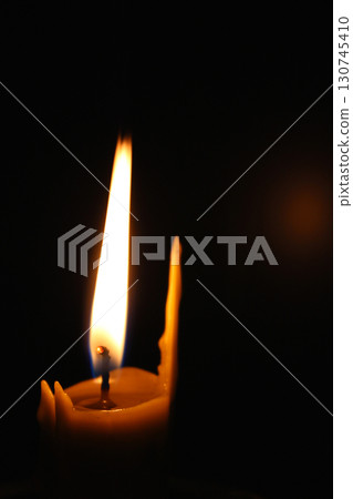 One waxy candle burns in the dark casting a red glow. Concept photo for mournful occasion One waxy candle burns in the dark casting a red glow. Concept photo for mournful occasion 130745410