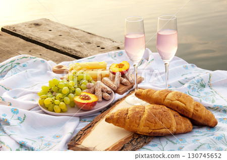 two glasses of champagne and fruit on a wooden platform near the water. picnic. two glasses of champagne and fruit on a wooden platform near the water. picnic. 130745652