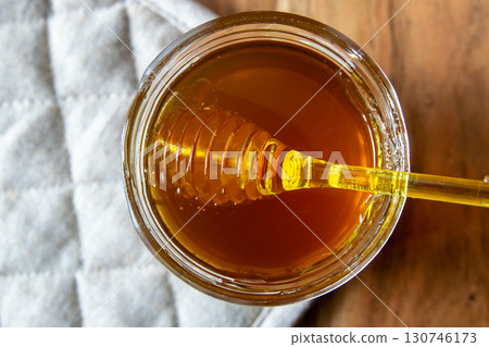 Honey big glass jar with honeycomb and yellow spoon stay on the wood table with rustic napkin. 130746173