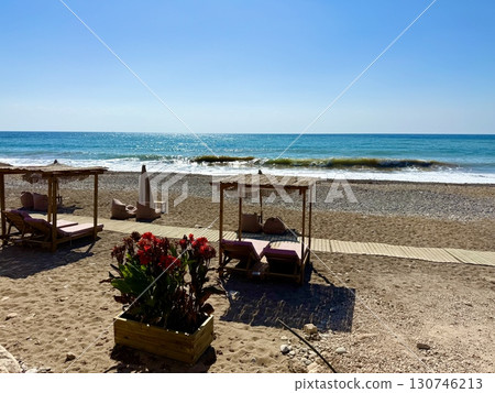 Public beach, summer, beautiful sunny weather. Picturesque beach, waves crashing on the sandy shore. Sea waves beat against the rocks. Cyprus Island, umbrellas, tourist boats, Mediterranean Sea. Public beach, summer, beautiful sunny weather. Picturesque beach, waves crashing on the sandy shore. Sea waves beat against the rocks. Cyprus Island, umbrellas, tourist boats, Mediterranean Sea. 130746213