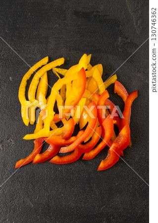 Fresh sliced red and yellow bell pepper strips on black slate background, top view 130746362