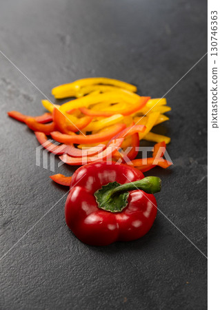 Sliced red and yellow bell peppers with whole pepper on black background, healthy food concept 130746363