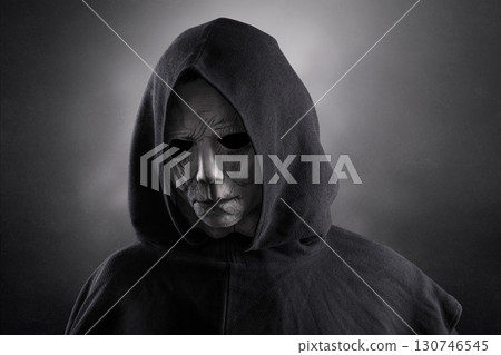 Portrait of a scary man in hooded cloak at night over dark misty background  130746545