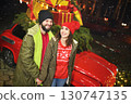 a couple of lovers - a man and a woman hold hands and smile against the background of a red retro car with Christmas gifts on the roof 130747135