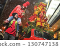 a young woman sits on the shoulders of a bearded man and smiles against the backdrop of a red retro car with Christmas gifts on the roof and against the backdrop of snow 130747138