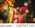 a couple of lovers - a man and a woman kiss against the backdrop of Christmas gifts and snowfall, holding sparklers in their hands 130747139