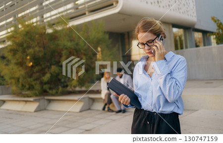A businesswoman engaged in using her smartphone while situated in a bustling urban setting 130747159