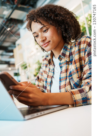 A young woman interacts with technology in a modern workspace, enjoying a cheerful atmosphere A young woman interacts with technology in a modern workspace, enjoying a cheerful atmosphere 130747165