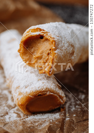 Caramel cream filled pastry rolls dusted with powdered sugar on parchment paper 130747272
