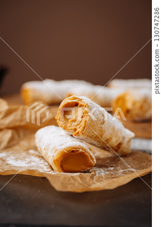 Caramel cream filled pastry rolls dusted with powdered sugar on parchment paper 130747286