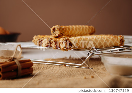 Close up of crispy wafer rolls with nut filling on rustic burlap and metal rack 130747329
