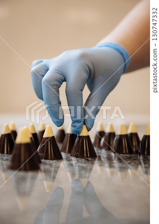 Chocolate cones with white tips being arranged by hand in a professional candy kitchen Chocolate cones with white tips being arranged by hand in a professional candy kitchen 130747332