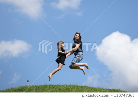 Mother and daughter happily jumping outside in summer Mother and daughter happily jumping outside in summer 130747365