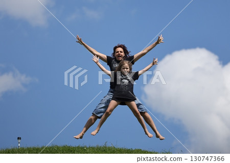Mother and daughter happily jumping outside in summer 130747366