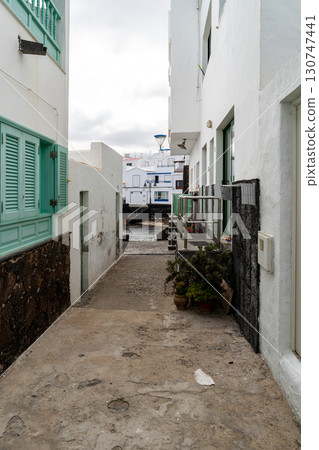 A narrow street in Punta Mujeres, Lanzarote, leads to the sea, flanked by white buildings and charming details. The area is a haven of tranquility. 130747441